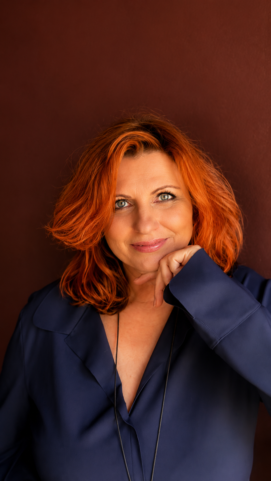 Mara Kaiser, Porträt in blauer Bluse vor warmem Hintergrund